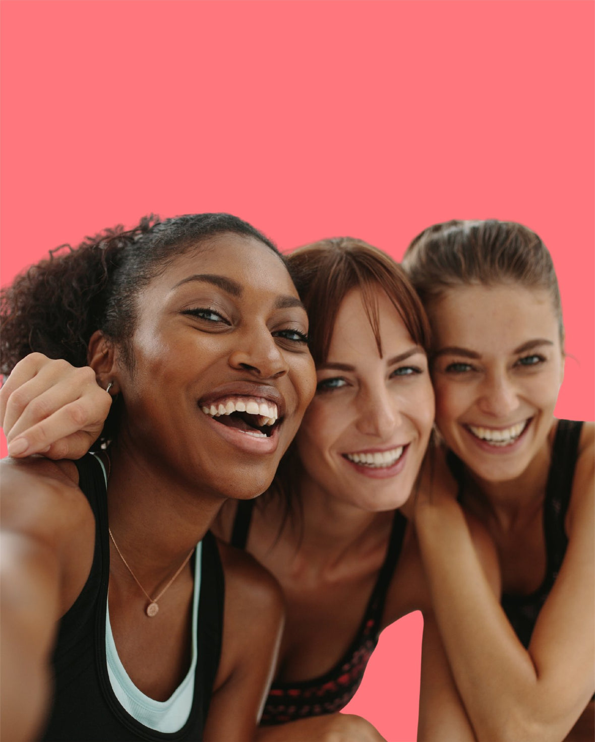 Three women in activewear laughing together against a coral background.